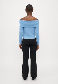 Off-shoulder ribbad ljusblå topp matchad med svarta utsvängda byxor. Toppen har långa ärmar och en figurnära design.