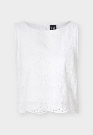 Blouse blanche sans manches en dentelle ajourée avec un ourlet festonné et un col rond, ornée de broderies florales et fermeture à boutons au dos.