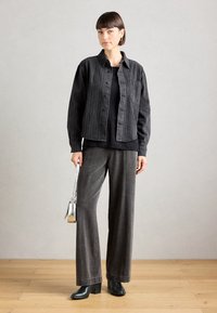 Chaqueta de mezclilla negra con rayas verticales, top negro y pantalones grises holgados. Combinado con botas negras de tacón cuadrado y un bolso plateado.