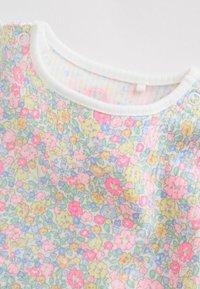 Vêtement doux pour bébé de couleur blanche avec un col rond et des boutons-pression, orné d'un motif floral coloré comprenant des fleurs roses, jaunes, bleues et vertes.