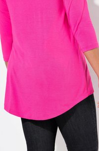 Fuchsia Langarmshirt mit abgerundetem Saum, weichem Material und seitlichen Schlitzen. Kombiniert mit dunklen Denim-Jeans, die ein lässiges Outfit präsentieren.