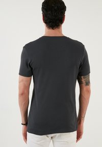 T-shirt carcunos închis, ajustat, cu mâneci scurte, textură ribbată și guler tip crew. Detalii de cusătură întărită la tiv și la mâneci.