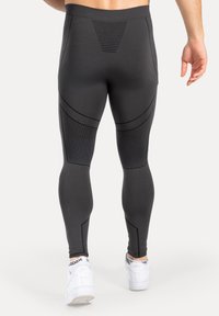 Schwarze Leggings mit figurbetontem Design, strukturiertem Rückenteil und kontrastierenden Nähten. Kombiniert mit weißen Sportschuhen.