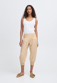 Pantalons cropped légers beige avec taille et poignets élastiques. Associés à un débardeur ajusté blanc. Des chaussures à enfiler décontractées complètent le look.