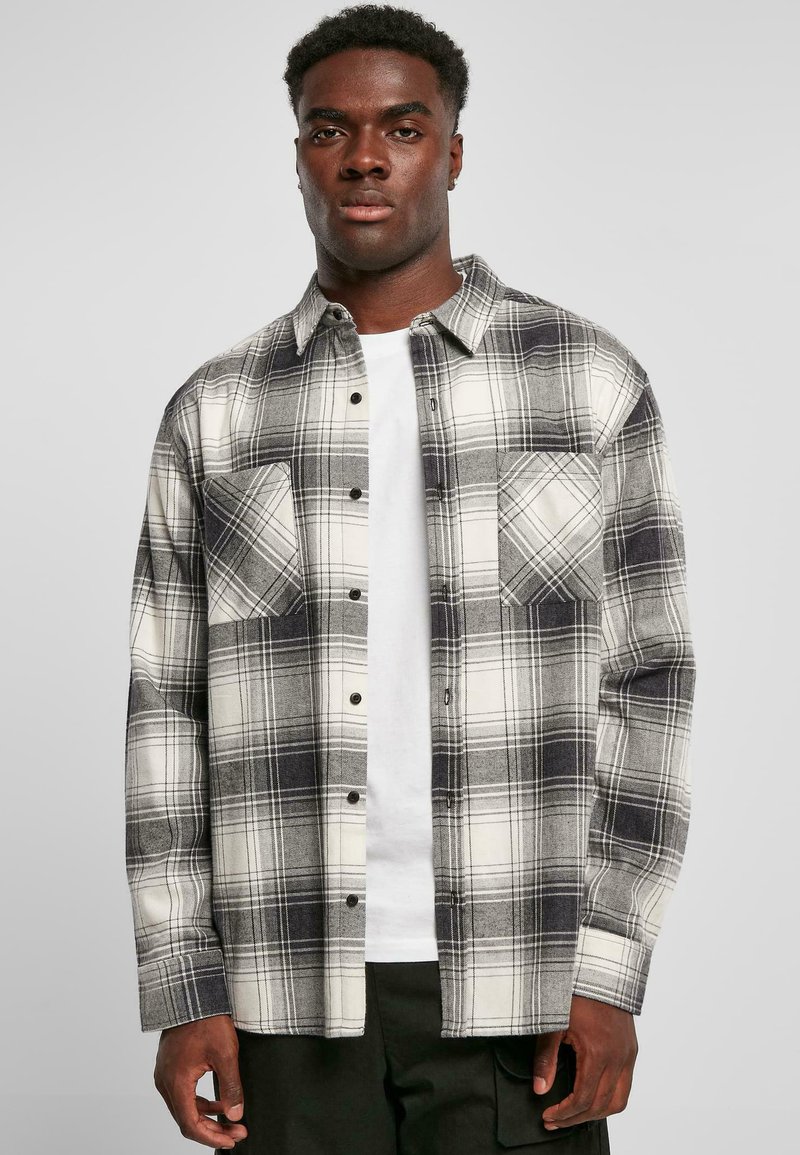 Flannel skjorte i sort og hvid plaid, lange ærmer, to brystlommer, knaplukning foran, båret over en hvid t-shirt. Blød tekstur.