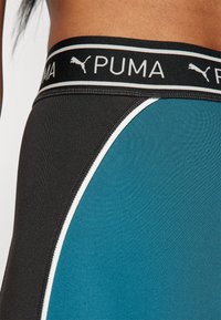 Leggings PUMA con un cinturino nero e un design a blocchi di colore blu e nero, evidenziato da piping bianco per contrasto e texture.
