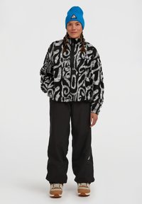 Fuzzy zwart-wit geblokte trui met hoge kraag, gecombineerd met losse zwarte broek en tan sneakers. Blauwe beanie met logodetail.