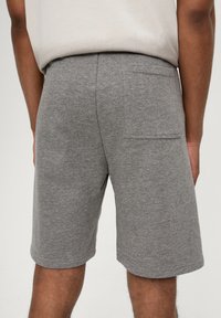 Grijze katoenen shorts met een zachte textuur, voorzien van een achterzak en een elastische tailleband. De zoom eindigt net boven de knie.