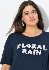 Námořnické tričko s krátkým rukávem, které zdobí bílý květinový aplikovaný nápis "FLORAL RAIN", kulatý výstřih, měkká látka a detail ohrnutého rukávu.