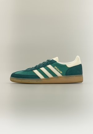 Baskets basses Adidas Spezial vertes et blanches avec semelle en gomme, trois bandes blanches, et étiquette "Spezial" sur le côté.