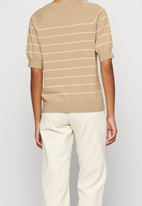 Suéter beige de punto con rayas horizontales color marfil, cuello redondo y mangas cortas abullonadas. Combinado con pantalones de pana color blanco roto.