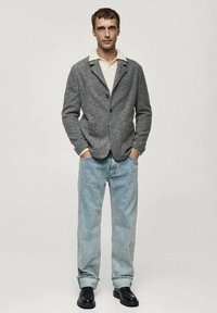 Gray wool blend blazer with a shawl collar, two front pockets, paired with light blue denim jeans and black leather shoes.