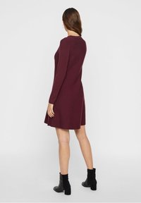 Burgunderfarbenes langärmliges Kleid mit einem ausgestellten Rock, Rückansicht. Aus weichem Stoff gefertigt, mit rundem Halsausschnitt und gerippten Bündchen. Schwarze Knöchelboots.