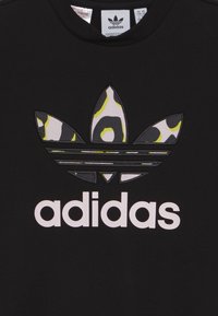 Svart sweatshirt med en strukturerad, flerfärgad leopardtryck Adidas-logga med vit skrift. Rundad nacke.