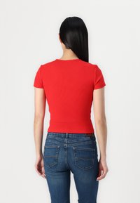 Haut rouge à manches courtes en maille côtelée avec un design ajusté, assorti à un jean en denim bleu foncé avec poches arrière et détails de couture.