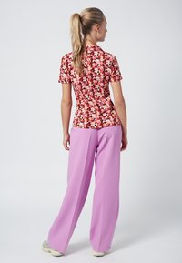 Floral short-sleeve top with a red background and multicolored flowers, paired with long, lavender wide-leg pants. Textured fabric and relaxed fit.