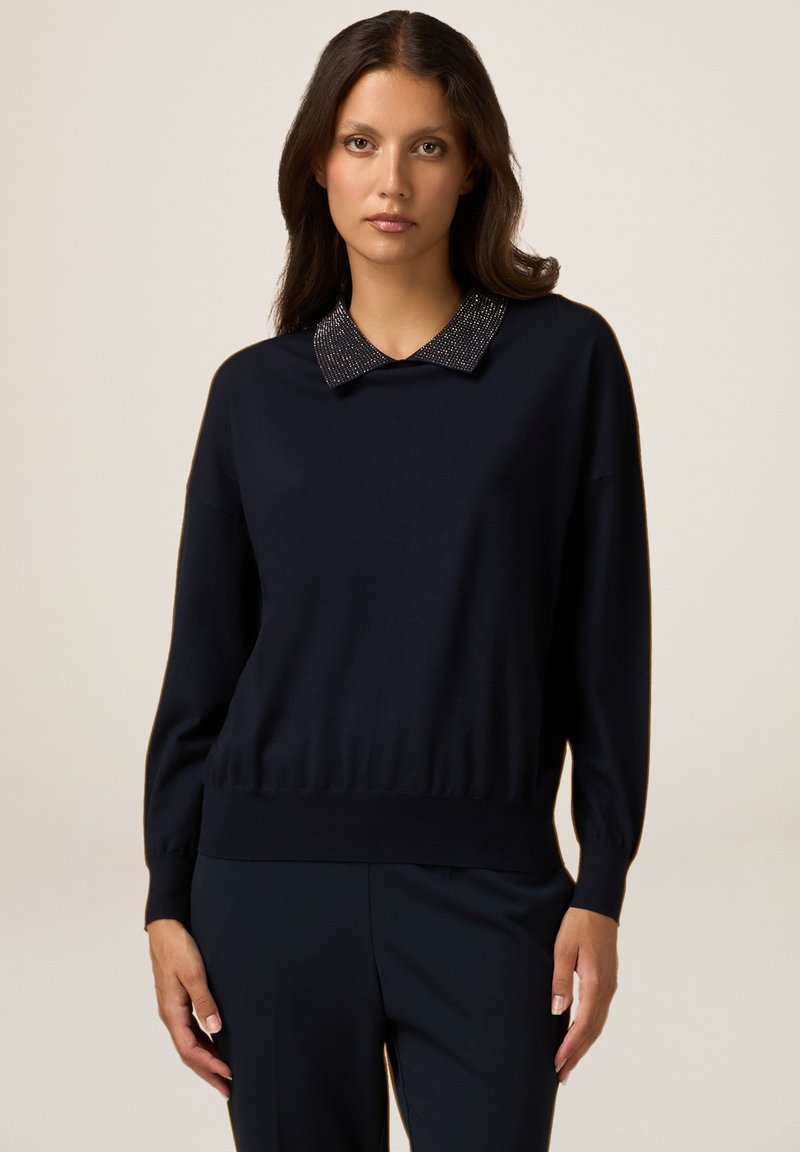 Suéter de cuello redondo en color navy con un cuello texturizado que presenta acentos metálicos. Tejido de punto suave con una cinturilla ajustada y mangas relajadas.