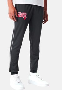 Schwarze Jogginghosen mit einem Chicago Bulls Grafik, weißen Seitenstreifen, gerippten Knöchelbündchen und glatter Textur. Kombiniert mit weißen Sneakers.