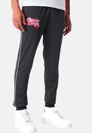 Sorte joggebukser med et Chicago Bulls grafisk motiv, hvide sidelister, ribbede ankelmanchetter og glat tekstur. Sammen med hvide sneakers.