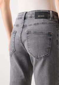 Grå denimjeans med høy midje, to baklommer med en karakteristisk form, og en svart "MOS MOSH"-label bak.
