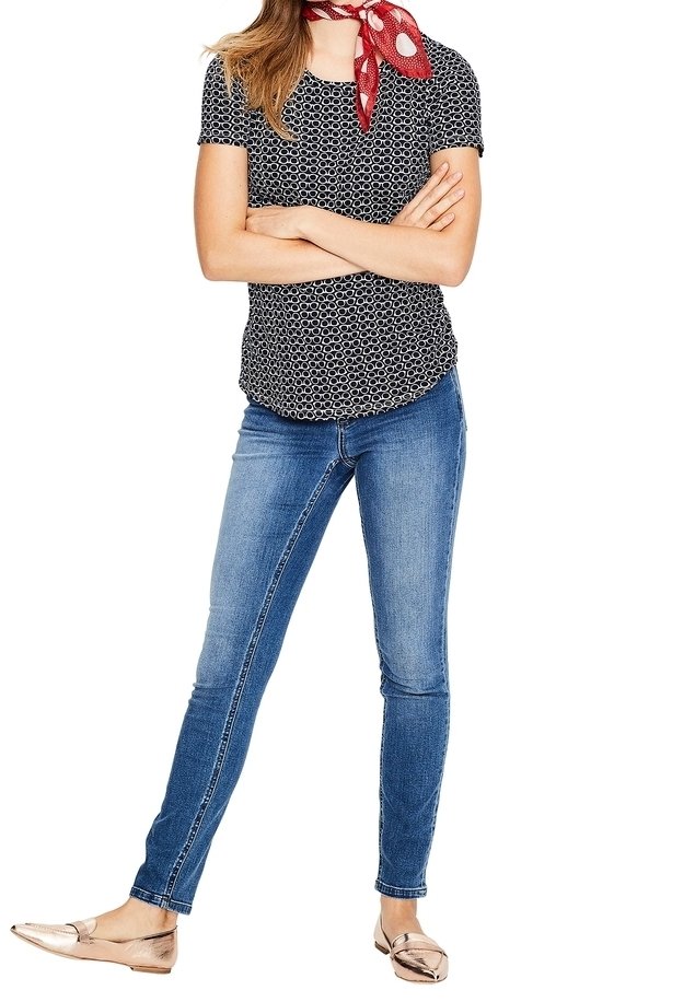 Svart kortärmad topp med vitt cirkulärt mönster, kombinerad med blå skinny jeans och metallisk rosé-guld platta skor. Röd prickig scarf som accent.