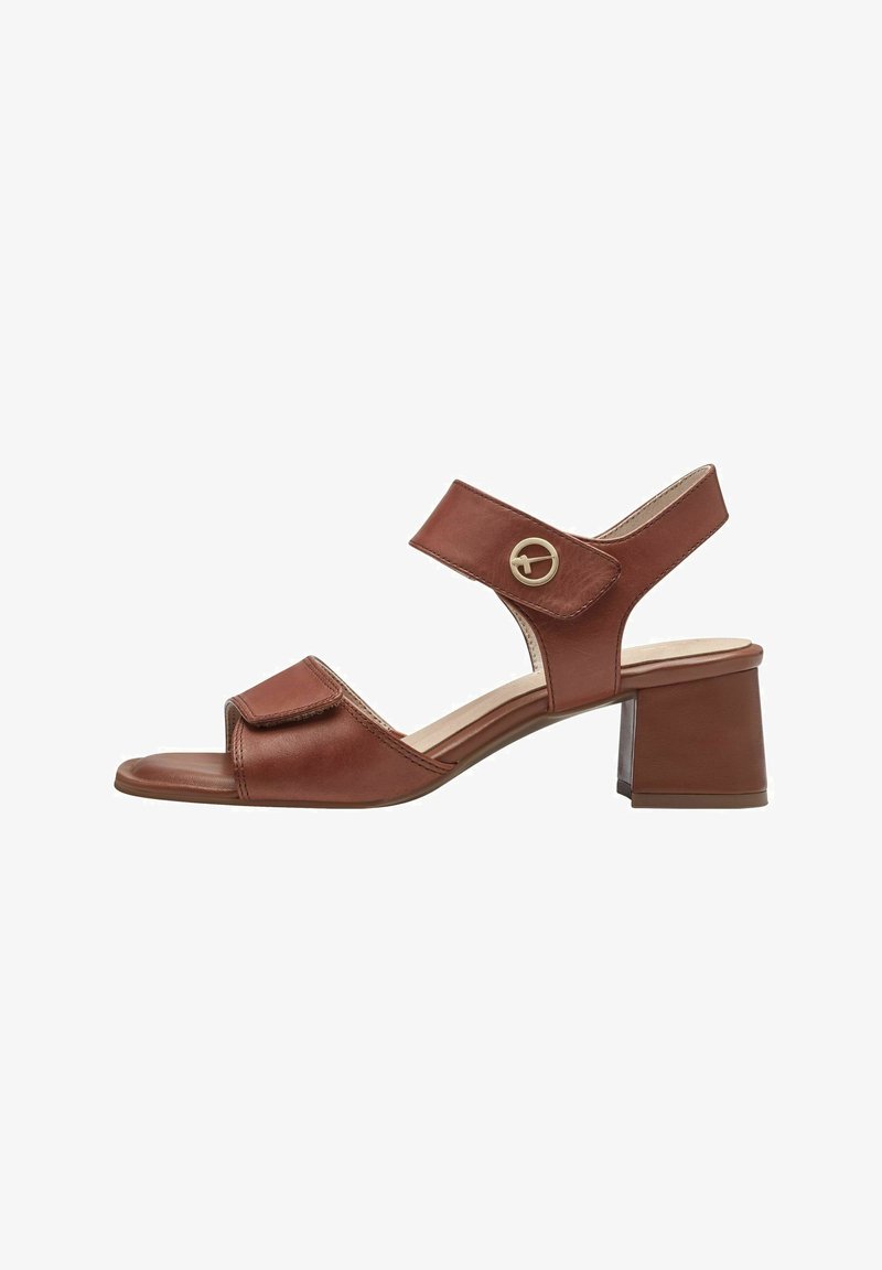 Sandale en cuir marron avec talon bloc, bride ajustable sur les orteils et la cheville, et boucle ronde en métal décorative sur la bride de la cheville.