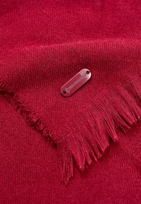 Scarf texturizzato di un profondo rosso con bordi frangiati e un'etichetta metallica impresso con "STEADY STATE". Materiale a maglia morbido.