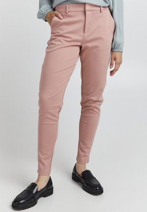 Růžové slim-fit kalhoty vyrobené z hladké látky, s plochým předním dílem, bočními kapsami a v kombinaci s černými mokasínami.