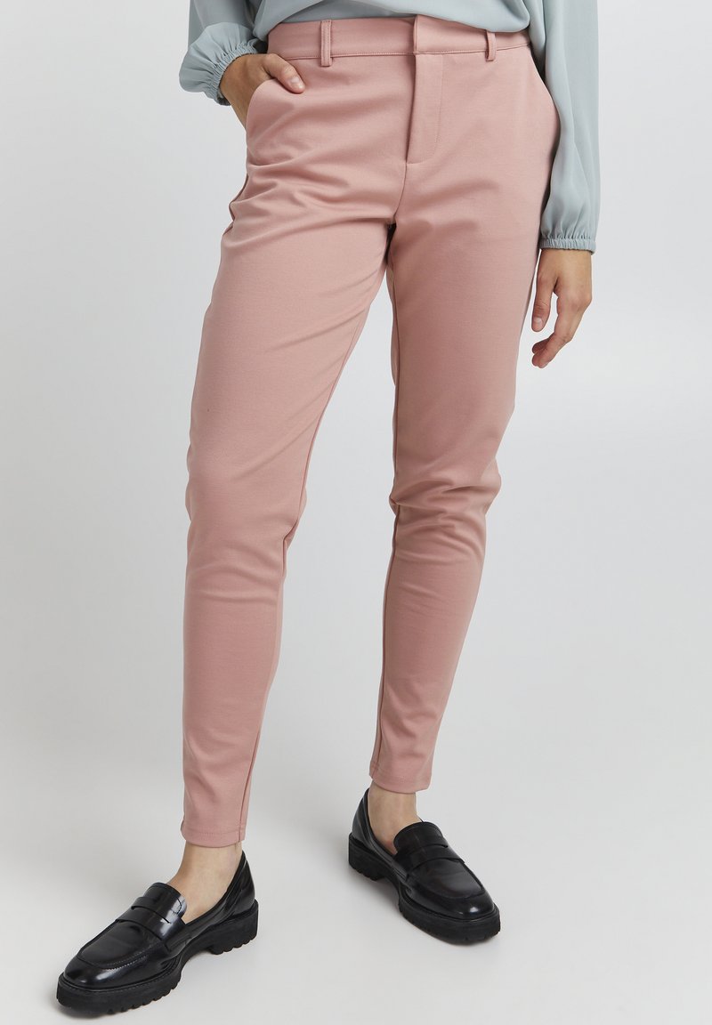 Růžové slim-fit kalhoty vyrobené z hladké látky, s plochým předním dílem, bočními kapsami a v kombinaci s černými mokasínami.