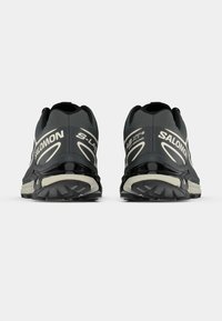 Fekete és szürke futócipők mintázott talppal, kiemelkedő logóval és elegáns dizájnnal. A hátoldalukon párnázott gallér található a támogatás érdekében.