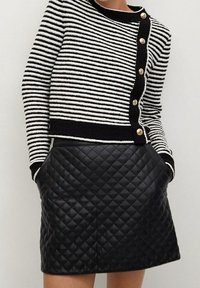Zwart-wit gestreepte cardigan met knopen en een gewatteerde zwarte leren minirok. De trui heeft een ronde hals en zakken.