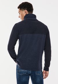 Námořnický svetr s vysokým límcem, strukturovanou horní částí a hladkým dolním dílem. Dlouhé rukávy a uvolněný střih.