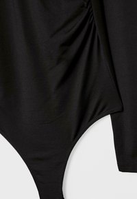 Schwarzes Langarmkleid mit gerafftem Stoffdetail und hoch geschnittenem Beinöffnungen auf einem schlichten weißen Hintergrund.