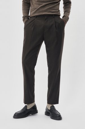 Brown pinstriped trousers with a tailored fit, featuring pleats at the front. Paired with dark loafers and light socks.