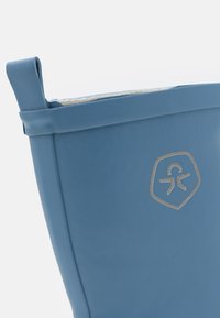 Seau en caoutchouc bleu avec une texture lisse et une forme arrondie. Présente un logo argenté sur le côté et une poignée robuste pour un transport facile.