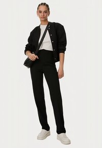 Svart bomberjacka över en vit topp, kombinerad med svarta byxor med hög midja och vita sneakers; har en minimalistisk design och rena linjer.