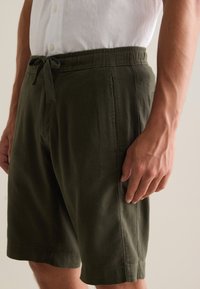 Pantaloni corti di cotone verde oliva con vita elasticizzata, caratterizzati da una vestibilità comoda e tasche laterali. Texture liscia con cuciture rifinite.