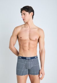 Navy boxer briefs with white repeating logo pattern, elastic waistband with "BOSS" branding, fitted design, and smooth cotton texture.