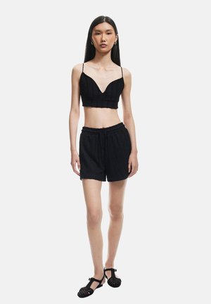 Sort crop top med dyb V-udskæring, parret med sorte shorts med snøre. Begge lavet af struktureret stof. Enkel design, ingen mønstre og minimal hardware.