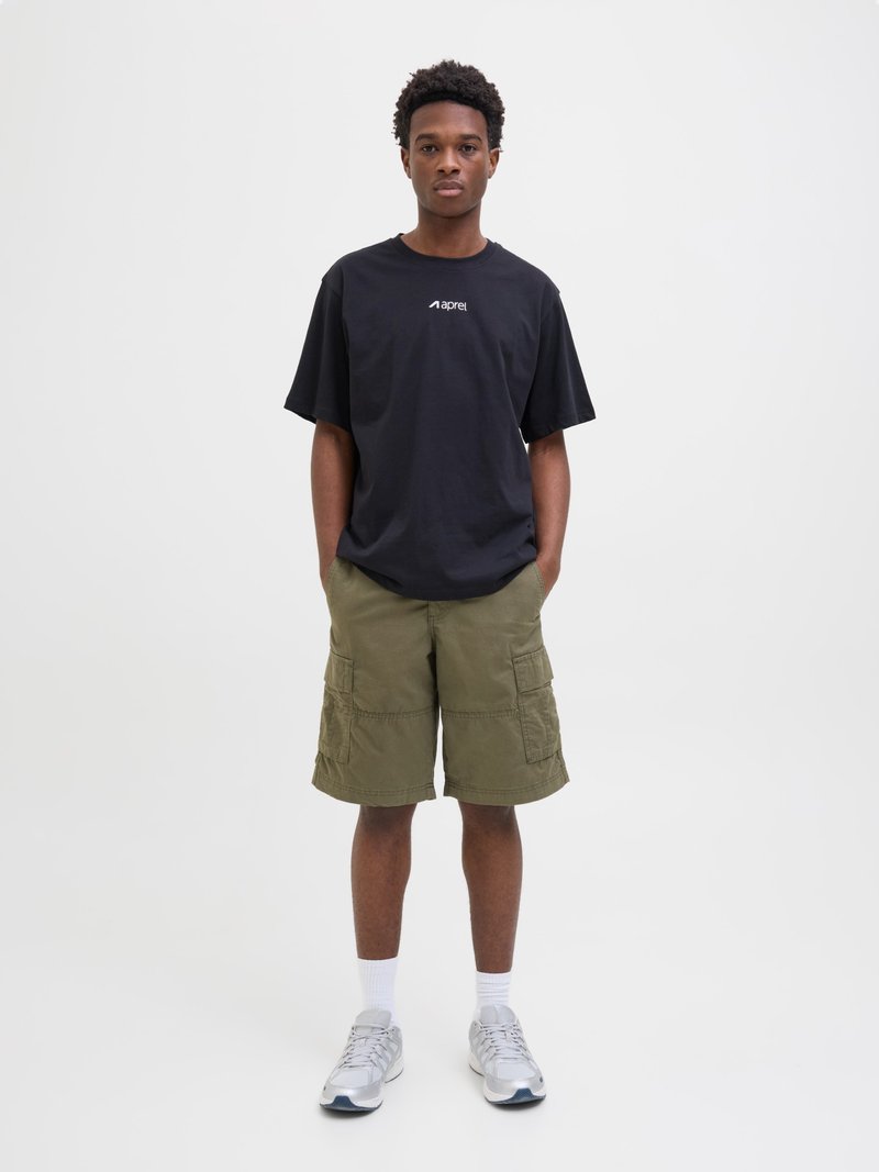 Black t-shirt with brand logo, green cargo shorts, white socks, and silver athletic shoes. Model stands with hands in pockets against a plain background.