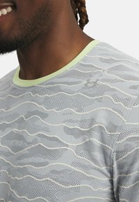 Vaaleanharmaa urheilupaita, jossa teksturoitu, aaltoileva kuvio, verkkoyksityiskohtia ja kontrastina vaaleanvihreä kaulus.