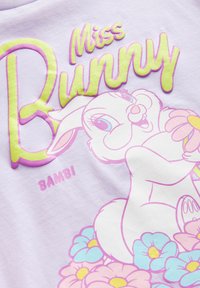 Hellblaues T-Shirt mit dem Text "Miss Bunny" in Gelb und Pink, umgeben von einer Grafik eines Kaninchens, das von bunten Blumen umgeben ist.