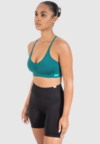 Teal vävda sportbehå i scoop-nacke med justerbara remmar, parat med högmidjade svarta shorts i slät tyg.