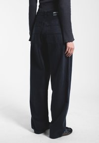 Mustat denim-housut leveillä lahkeilla ja korkealla vyötäröllä, joissa on kaksi takataskua ja merkki vyötärökaistassa. Sileä pinta ja rento istuvuus.