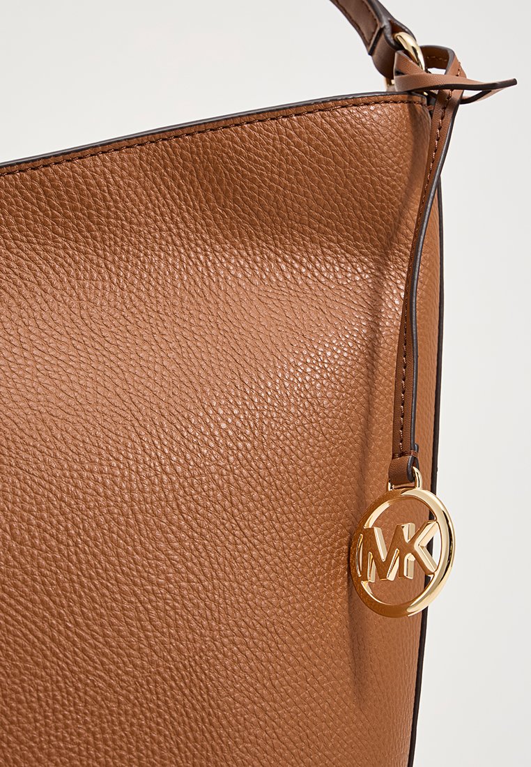 Bolso de mano de cuero marrón con una superficie texturizada, una parte superior recta y un charm en forma de círculo dorado en el lado.