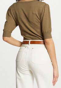 Top de punto verde oliva con mangas cortas abullonadas, combinado con jeans blancos de tiro alto y un cinturón marrón. Textura suave y estilo ajustado.