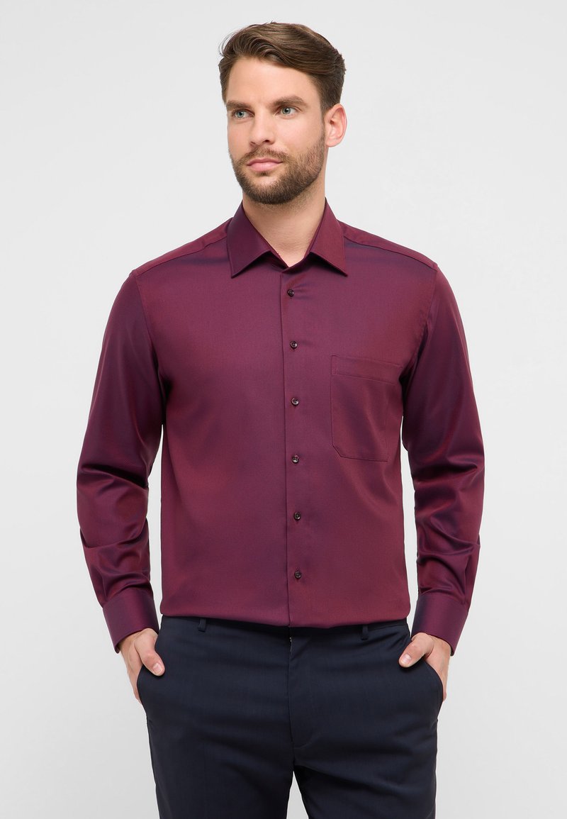 Camicia bordeaux a maniche lunghe con colletto appuntito, taschino frontale e chiusura con bottoni; tessuto liscio con una leggera lucentezza.