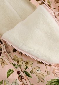 Tela de forro polar rosa con patrones de flores y ositos. El forro interior es de suave forro polar blanco. Presenta un cierre con cremallera con detalles a juego en rosa.