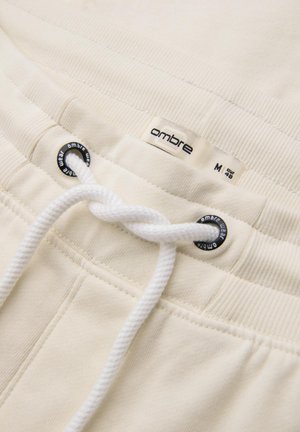 Pantalons de survêtement blancs en coton, avec un cordon de serrage, une taille côtelée et une étiquette portant la marque "ombre" près du haut.