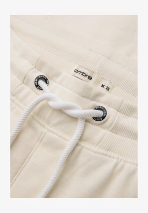 Pantalons de survêtement blancs en coton, avec un cordon de serrage, une taille côtelée et une étiquette portant la marque "ombre" près du haut.